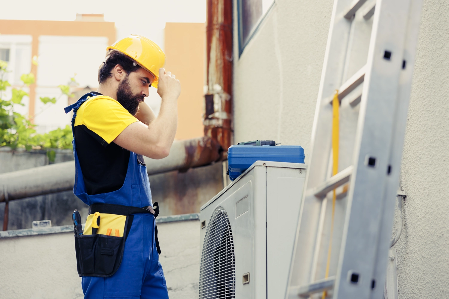 Elektro Wollmer GmbH - Innovative Klimatechnik - Ein Klimatechniker in Arbeitskleidung überprüft die Dachklimaanlage mithilfe eines Tablet-Computers. Der Fachmann trägt Brille und Kappe. Er hält das Gerät in der Hand und arbeitet bei bewölktem Himmel an der Klimaanlage im Außenbereich des Gebäudes.